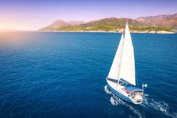 Sailboat heeling in the wind near a green island at sunset