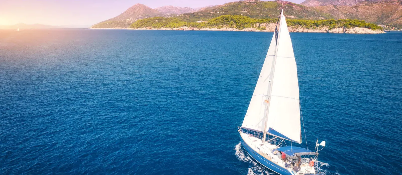 Sailboat heeling in the wind near a green island at sunset