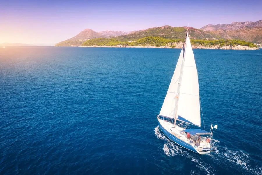 Sailboat heeling in the wind near a green island at sunset