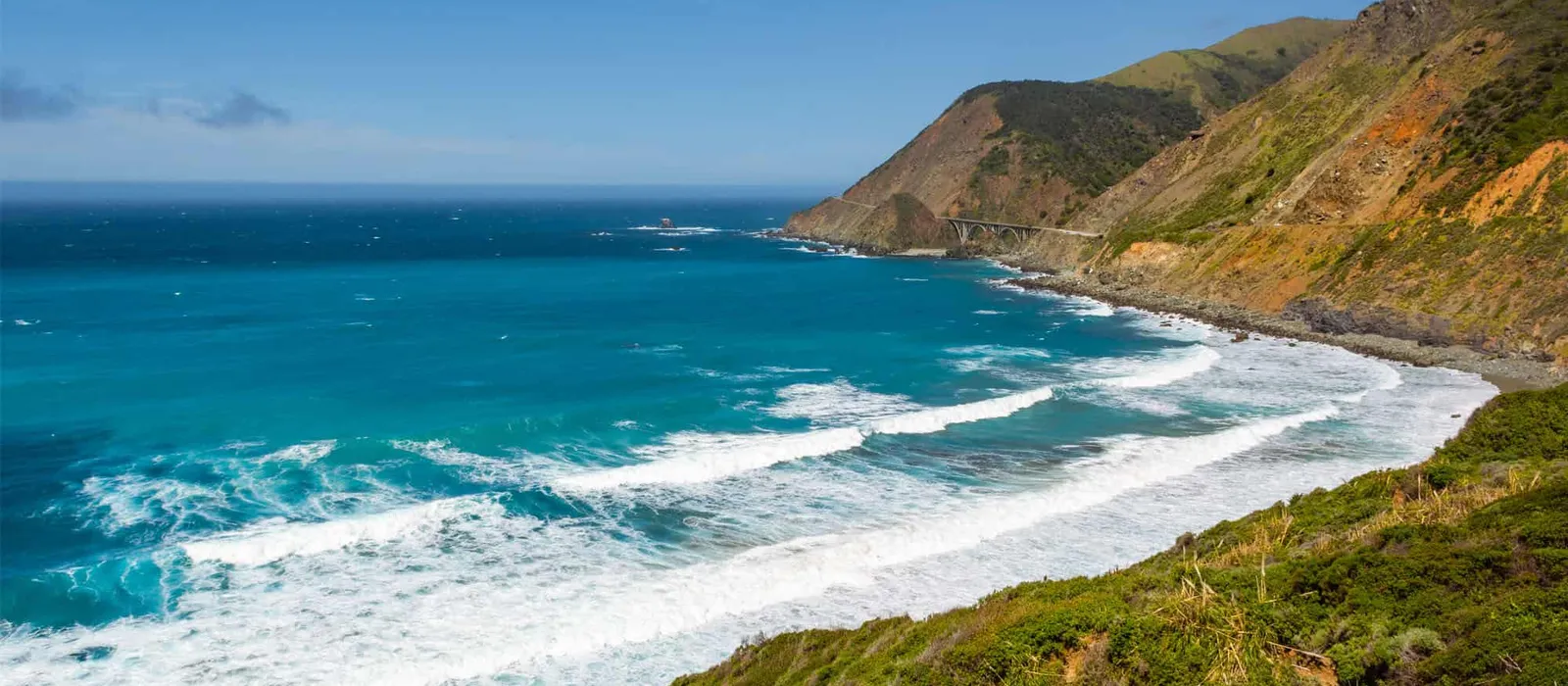 Surf rolling into a cove below green hills