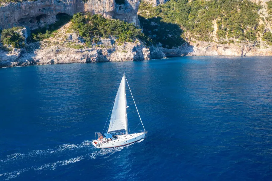 Sailboat under sail along a white cliff coast, seen from above