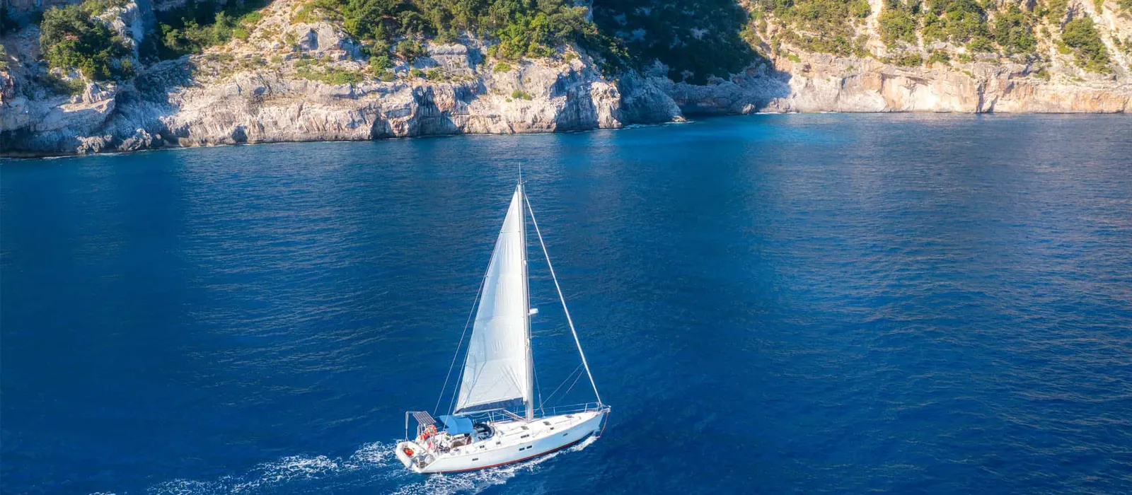 Sailboat under sail along a white cliff coast, seen from above