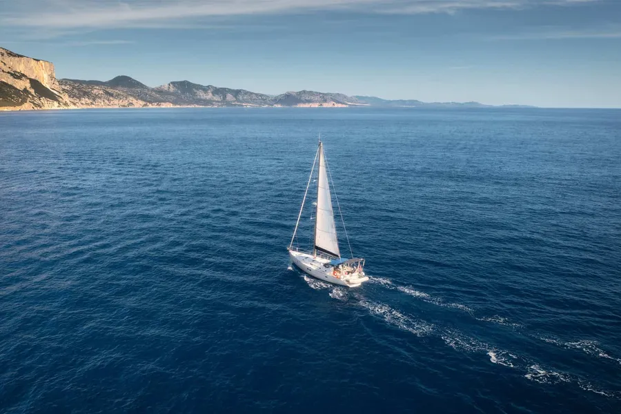 Sailboat crossing deep blue water near the coast, seen from above