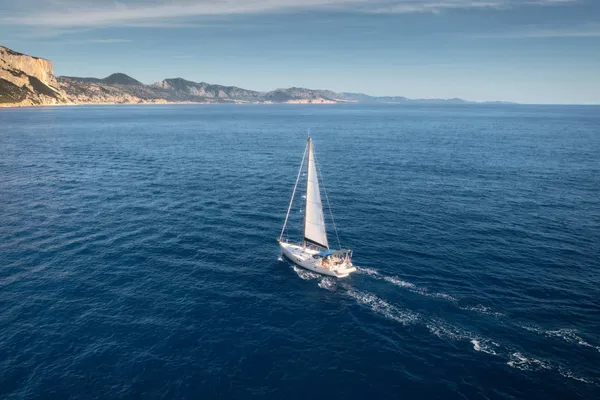 Sailboat crossing deep blue water near the coast, seen from above