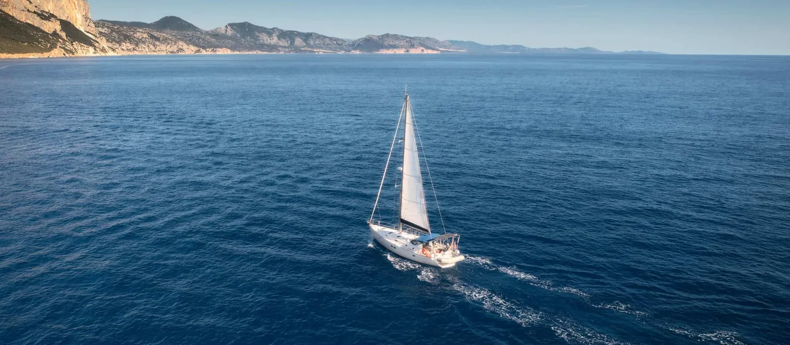 Sailboat crossing deep blue water near the coast, seen from above